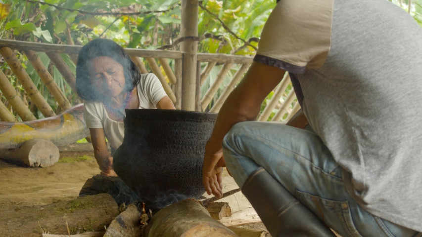 indigenous old woman blowing the fire on amazonian village in ecuador