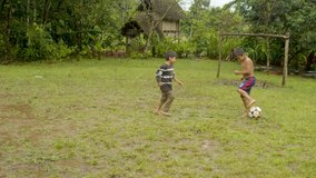 two young indigenous boys are playing football on a muddy pitch somewhere outside in their rural village older boy scores a goal general shot camera follow up camera movement in ecuador - Powered by Shutterstock - Get 15% off with code: PIKWIZARD15