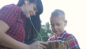 happy family funny slow motion video teamwork outdoors. Mom and son listen to music on smartphone in the same headphones for two . happy family mother woman and son little boy spend time in lifestyle