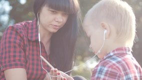 happy family funny slow motion video teamwork outdoors. Mom and son listen to music on a smartphone in the same headphones for two. happy family mother girl and son little boy lifestyle spend time in
