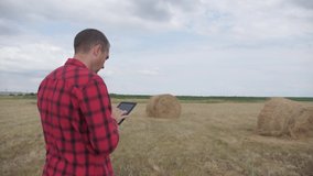 smart farming agriculture concept. man farmer studying a haystack in a field on lifestyle a digital tablet. slow motion video. male agronomist botanist farmer working in the field