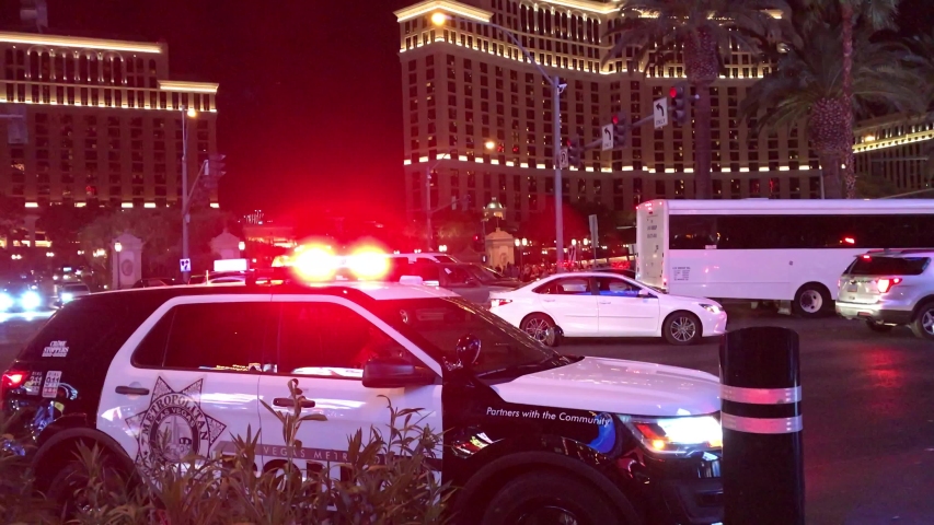 LAS VEGAS, Aug 16th, 2019: Police car with flashing lights on Las Vegas Strip in front of the Bellagio Hotel and Casino, with officer sitting inside and traffic passing by. With ambient sound.