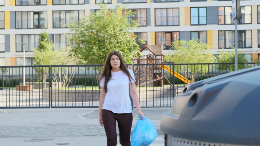 Young woman throws a bag of garbage into the tank near the house.