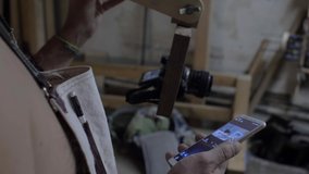 a carpenter in a working apron sets up a photo device through the application in the phone. man controls the camera through the phone. 4k. 4k video. 60 fps