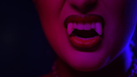 Sexy Vampire Woman's red bloody lips close-up. Vampire girl licking fangs with tongue. Fashion Glamour Halloween art design. Close up of female vampire mouth, teeth. On black background 4K UHD video