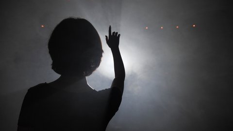 black silhouette of young woman walking to light spot through fog clouds and hand hides bright disk slow motion