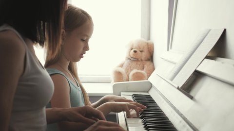 Mother teaching daughter to play piano at home.