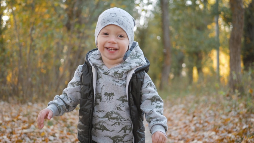 Happy baby boy running in autumnal park. Little child playing on autumn walk. Autumnal forest with golden leaves. Steadicam video, 4K slow motion.