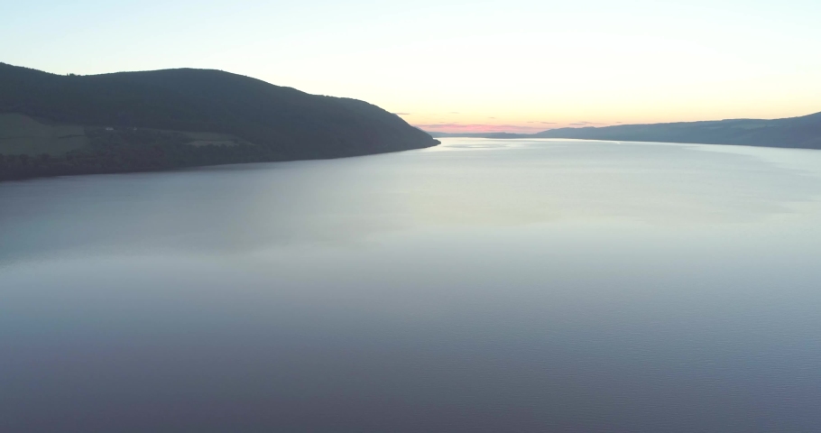 Aerial reveal of Urquhart Castle ruins from above the waters of Loch Ness in the Scottish Highlands at dawn