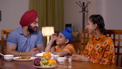 Happy Sikh Punjabi family having lunch together in a dining room - family concept. Loving family having breakfast and spending time together, looking towards the camera - Love and bonding