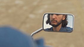 Cropped view of handsome young brunet bearded man looking at the mirror and fixing his hair while sitting on motorcycle at the beach