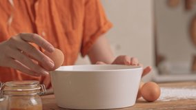 Cropped view of young woman smashing eggs into the bowl while cooking at the kitchen