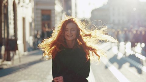 Charming red hair young woman in green sweater walks in the city center and then turns to the camera and smiles feel happy the sun shines