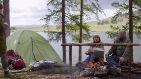 Senior tourist couple walking to friends sitting by campfire, smiling and chatting with them over tea on autumn day in the forest - Powered by Shutterstock - Get 15% off with code: PIKWIZARD15
