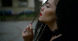 young woman holds curly hair lock over nose and lips closeup