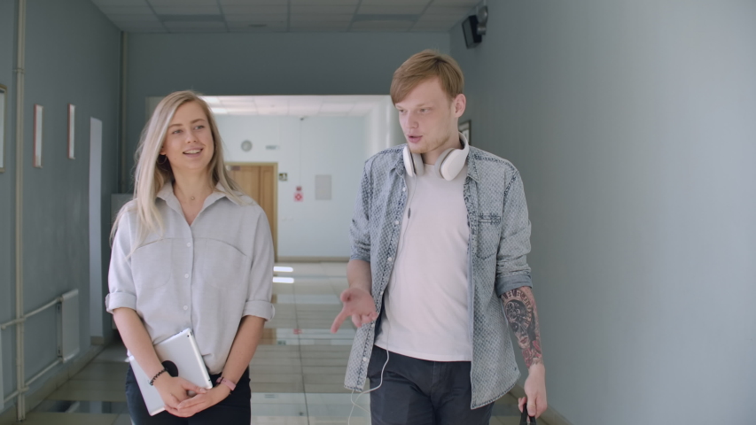 A guy and a girl walk along the college corridor and laugh and talk