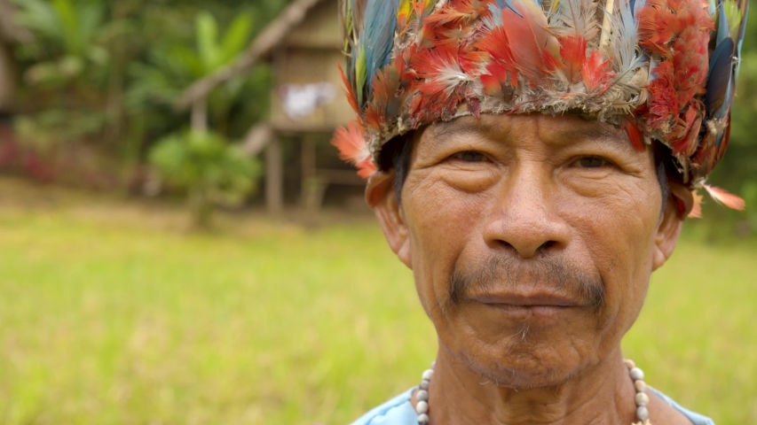 portrait of an old indigenous amazonian man standing in his village wearing traditional outfit and a colorful hat slow- motion closeup shot in ecuador Royalty-Free Stock Footage #1037959673