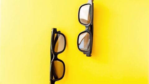 Stop motion animation of view from above of two pair 3D black glasses dan?ing with each other on yellow background