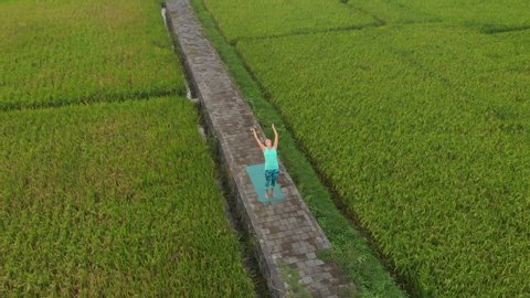 Aerial Slowmotion shot of a young woman practicing yoga on a beautiful rice field
