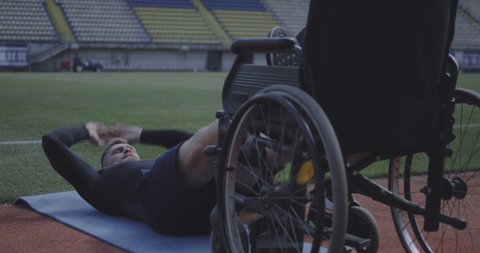 Full shot of a disabled male athlete doing sit ups while being encouraged by trainer