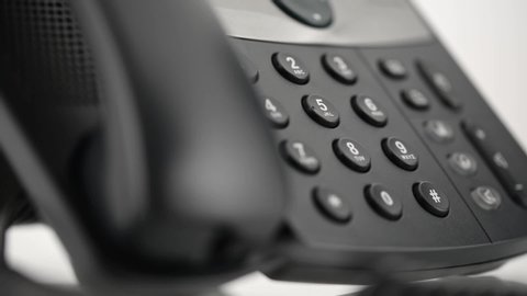 Low angle closeup view of male hand picking up handset and dialing telephone number on black landline phone keypad.