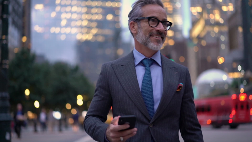 Slow motion of smiling mature lawyer in expensive suit messaging with customers via cellular device while walking in financial district,successful businessman in optical eyewear searching trading news | Shutterstock HD Video #1037982434