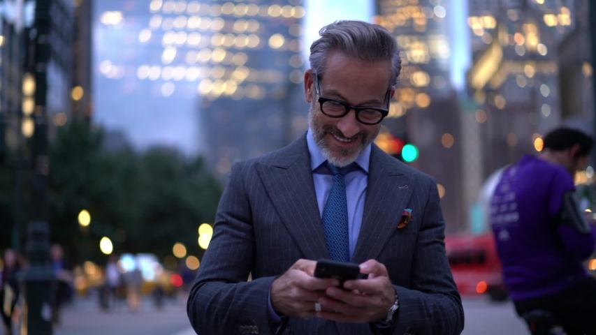 Successful male entrepreneur in elegant suit walking at metropolitan street in downtown and smiling during online messaging via smartphone device, slow motion effect of confident employer | Shutterstock HD Video #1037983109