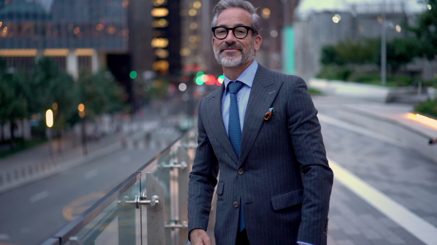 Slow motion of successful mature entrepreneur in expensive clothing posing in financial district with crossed hands and sincere smile on face, happy middle aged banker standing at urban setting  | Shutterstock HD Video #1037983649