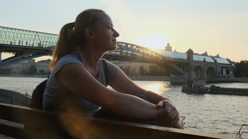 Portrait of  happy woman at sunset on background of river in evening city.