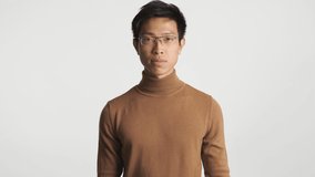 Young serious asian man in eyeglasses disappointedly showing whatever gesture and leaving shot isolated. No matter expression