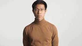 Young serious asian man in eyeglasses asking again and answering no on camera. Not hear gesture