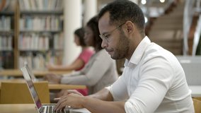 Side view of focused young man using laptop at library. Handsome African American student studying at library. Education concept