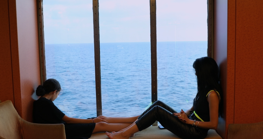 Mom and daughter are enjoying themselves in front of the Cruise Ship window while sailing.
