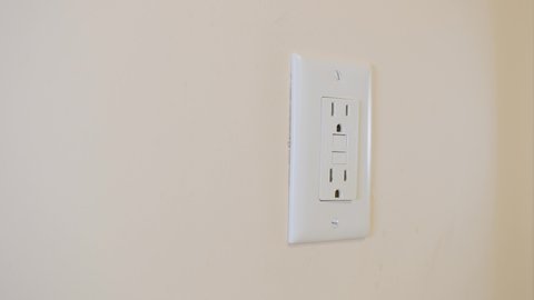 Close up of male hand resetting tripped GFI electricity receptacle. Residential ground fault interrupter electric socket plug and wall plate.