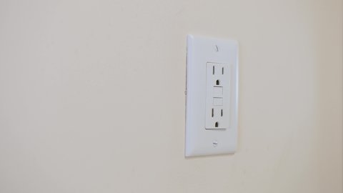 Close up of male hand inserting and testing cord with GFI plug into electricity receptacle. Residential ground fault interrupter electric socket plug and wall plate.