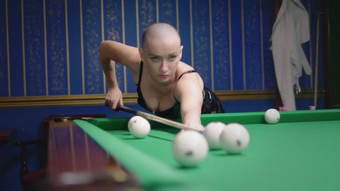 stylish bald girl in a black leather corset plays billiards.