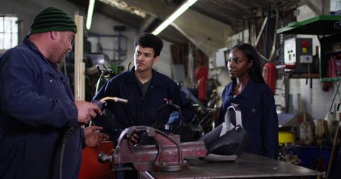 4K Young mechanics learning welding skills from experienced coworker in garage workshop