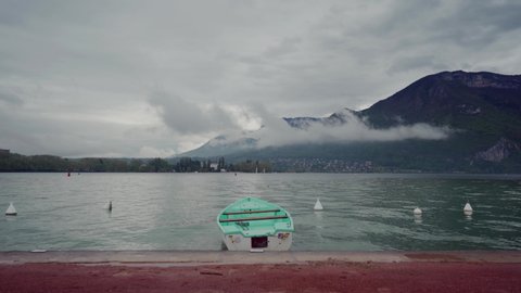 Lonely mint boat moored to promenade of Lake Annecy on fog mountains background in rainy day