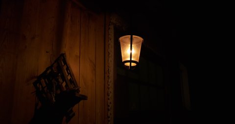 Iron lantern swaying in wind, night light, shadows on wooden wall of rustic barn. lonely lantern on dark street, wind sways, shadows run along wooden wall, ominous atmosphere, warm light of lantern