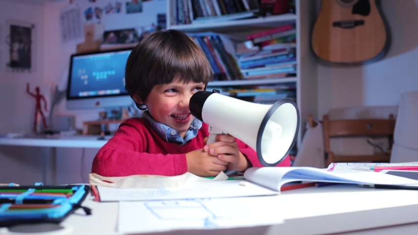 portrait of a boy in red clothes sitting at a table smiling then shouting into a megaphone Royalty-Free Stock Footage #1038027737