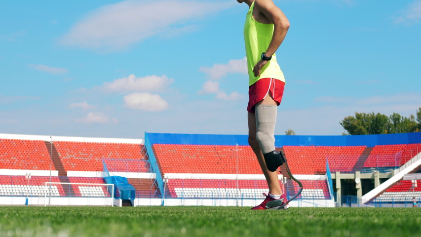Athlete with an artificial leg is stretching at the stadium