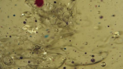 Splash in the gold liquid on the background of black, red, violet and transparent floating bubbles. Color drops in the transparent cup. Close up. Slow motion.