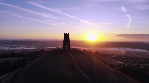 Aerial pan of Glastonbury Tor at sunrise, with a deep morning blue sky.