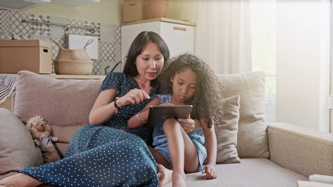 Mother and Daughter having fun on a digital tablet in a home interior. A cute happy mother and daughter using a digital tablet at home in the living room.