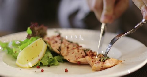 Men's hands with a fork and knife. A man is eating trout or salmon steak in a restaurant. Fish menu.