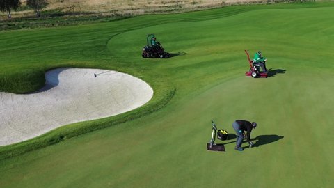 Special staff with professional equipment prepare golf field, cutting green grass, add new golf holes, cleaning the sand in bunkers for the new game season.