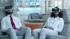 Smiling young colleagues in vr headsets. Professional African American business people sitting on chairs and using virtual reality headsets in modern office. Business and innovation concept