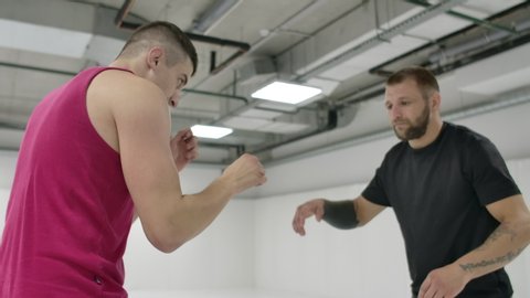 MMA fighters practice wrestling techniques. White hall and wrestlers on the tatami. A man in a red T-shirt and a man in a check T-shirt. Coach and fighter practice captures and throws