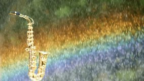 Golden alto saxophone on the background of a bright beautiful multi-colored rainbow on a background of summer rain. Rainbow flag for LGBT communities. Saxophone in the rainbow rain. Slow motion video.