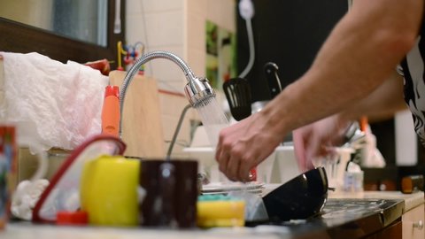 a man washes dishes, next to a large pile of dirty dishes. Close-up of hands, no face, selective focus
